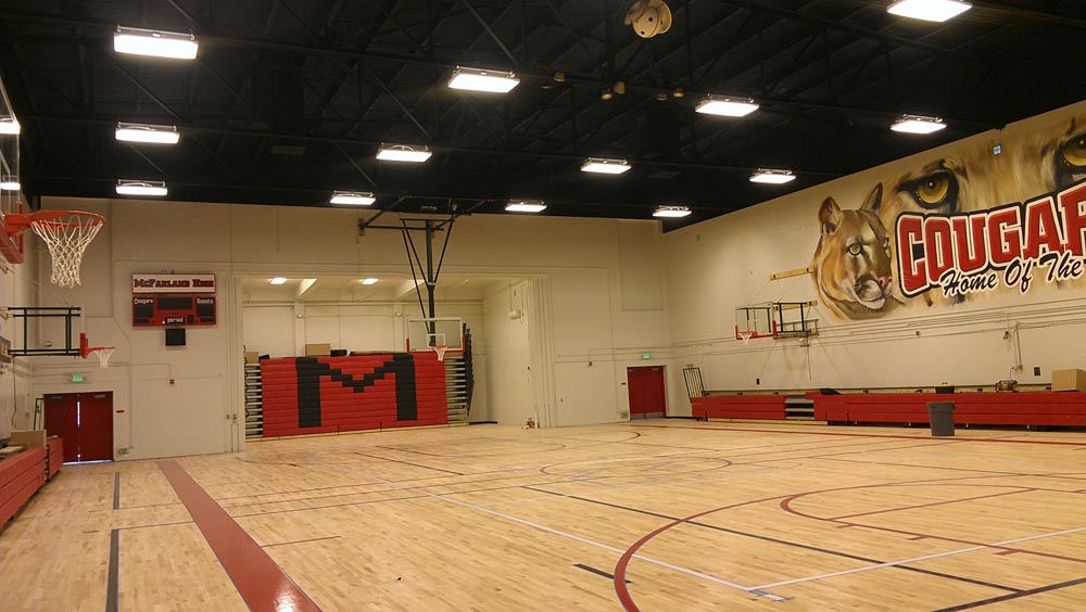Empty school gymnasium with basketball hoops, polished hardwood floor, red bleachers and large cougar mural on wall