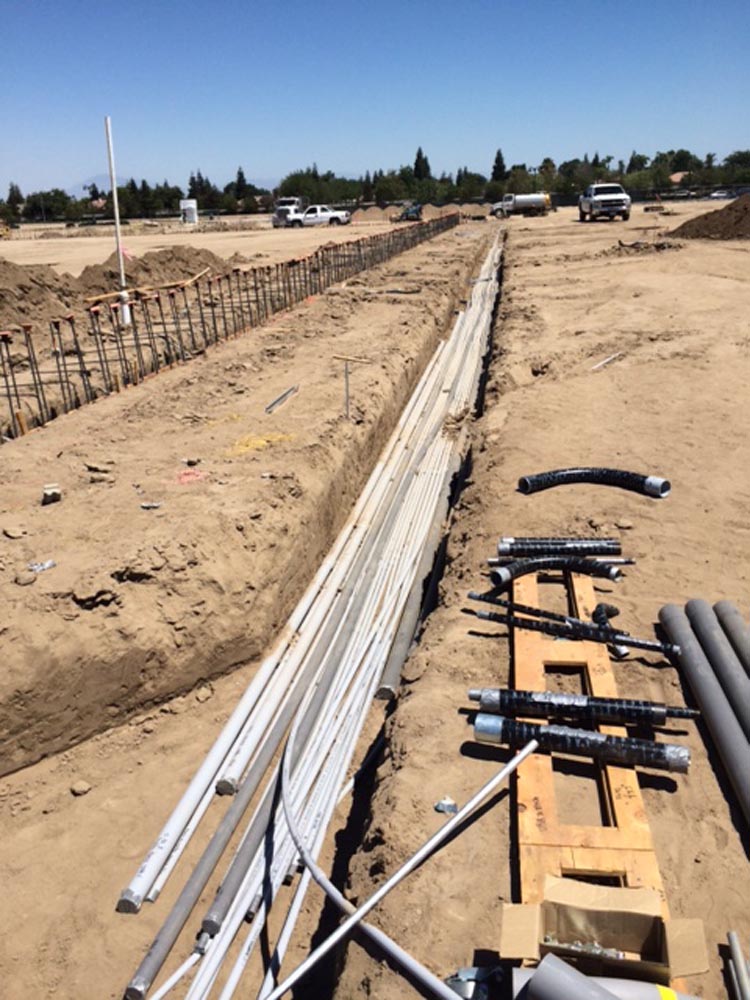 Construction site trench with bundled electrical conduits and PVC pipes laid for underground utilities