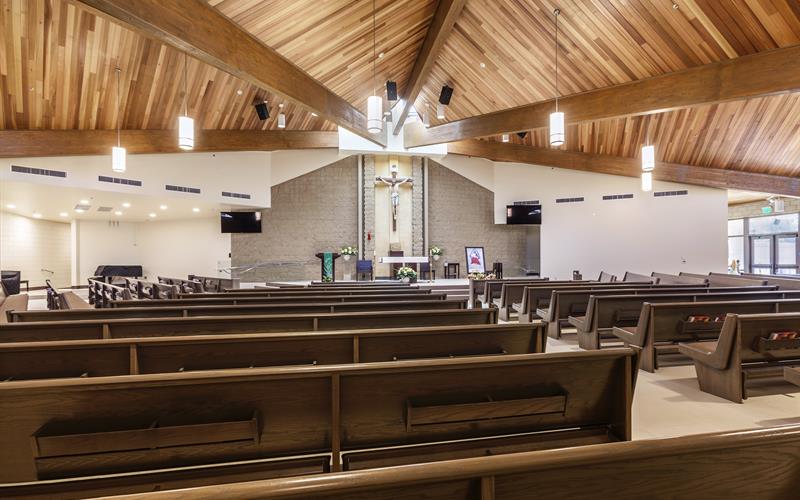 Empty modern church interior with wood-paneled vaulted ceiling, rows of wooden pews and altar featuring a crucifix