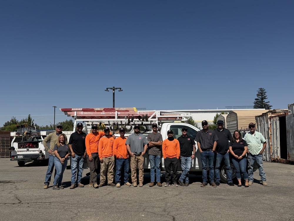 Group of construction workers and staff in safety gear standing in front of service trucks with ladders under clear blue sky